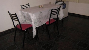A dining area with a table covered in a white tablecloth, four chairs with red cushions, and a small vase with flowers. - Guatambú Apart Hotel (Puerto Iguazú)