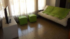 Ein Zimmer mit einem Bett, einem Fernseher auf einem Schrank und zwei grünen Hocker.