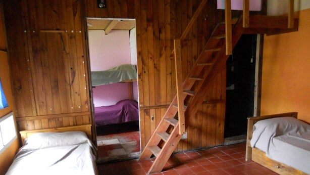 Ein rustikaler Raum mit Holzwänden, einem Stockbett, einem Einzelbett und einer Holztreppe.
