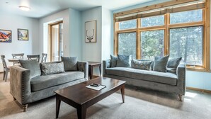 A living room with two grey sofas, a wooden coffee table, and a large window with a view of trees. - Modern Ideal Ski Location, Views, Heated Garage, Elevator 633 (Mammoth Lakes)