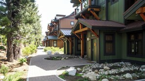 A row of multi-story buildings with balconies, a paved walkway, and a landscaped area with rocks and shrubs. - Modern Ideal Ski Location, Views, Heated Garage, Elevator 633 (Mammoth Lakes)
