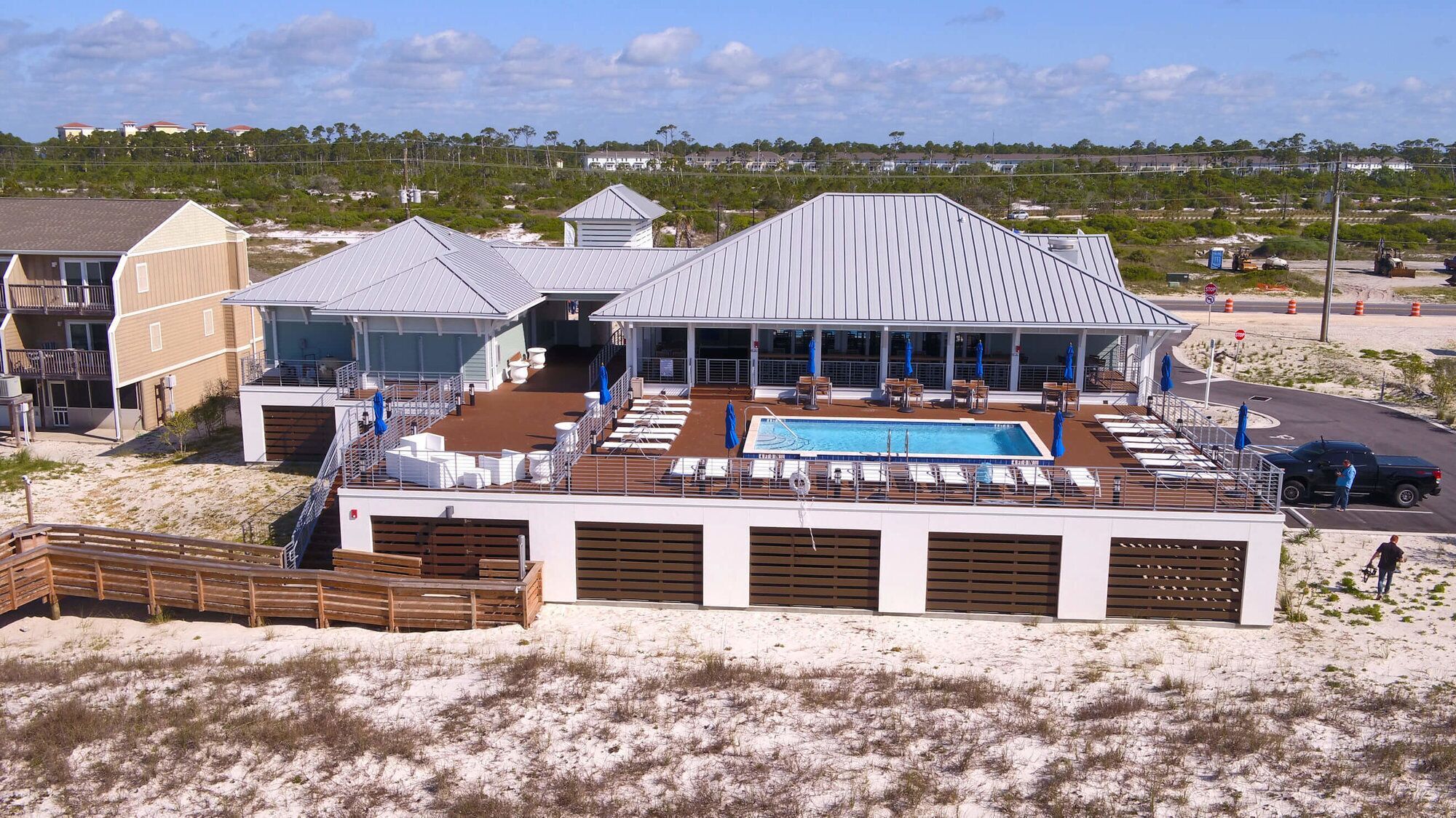 A beachside building with a pool, outdoor seating, and a wooden deck.