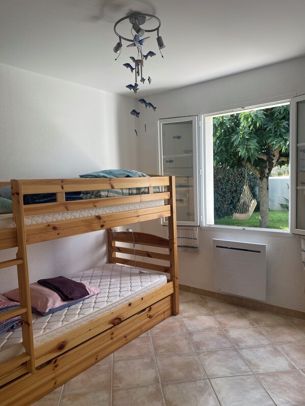 A room with a bunk bed, a ceiling fan, a window with a view of greenery, and a radiator.