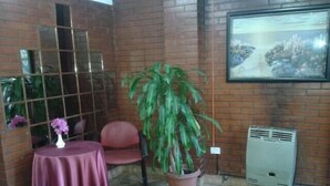A corner room with a brick wall, a window with a grid pattern, a table with a purple tablecloth, a chair, a potted plant, and a wall-mounted air conditioner. - Hotel Colonial (Buenos Aires)