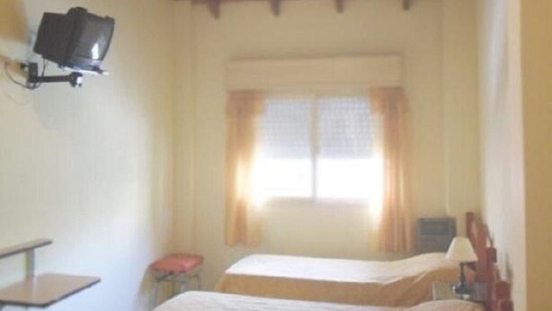 A room with two beds, a television, a window with curtains, and a wooden ceiling. - Hotel Colonial (Buenos Aires)