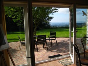 A patio with a table and chairs, a view of a grassy area, and a distant landscape. - Panorama Vacation Rental - Idyllic Location with Panoramic Views (Schaufling)