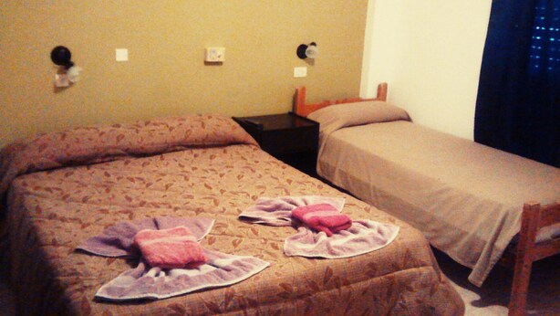 A double bed with a patterned bedspread and two towels. There is a nightstand with a lamp and a small table beside the bed. - Hotel Bahía Del Sol (San Clemente)