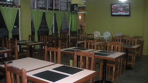 A restaurant with wooden tables and chairs, green curtains, and a television on the wall. - Hotel Bahía Del Sol (San Clemente)