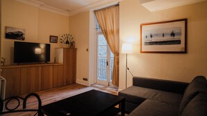 Una sala de estar con televisión, sofá, mesa de centro y lámpara.