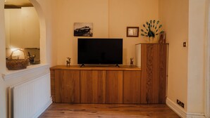 Una sala de estar con un mueble de madera para entretenimiento, un televisor y una decoración con motivos de pavo real.
