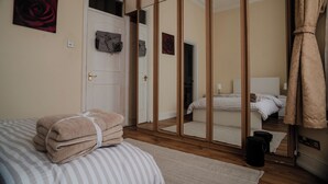 Un dormitorio con cama, espejo, puerta y una pila de toallas.