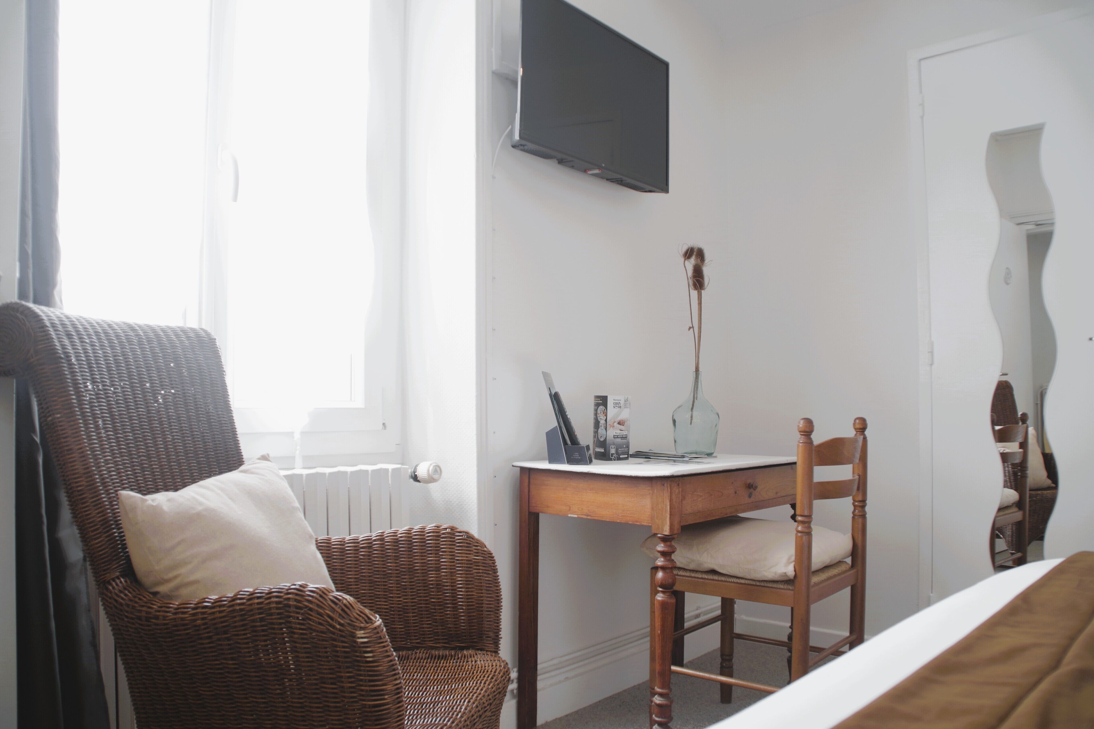 A room with a wicker chair, a wooden desk, and a television on the wall.