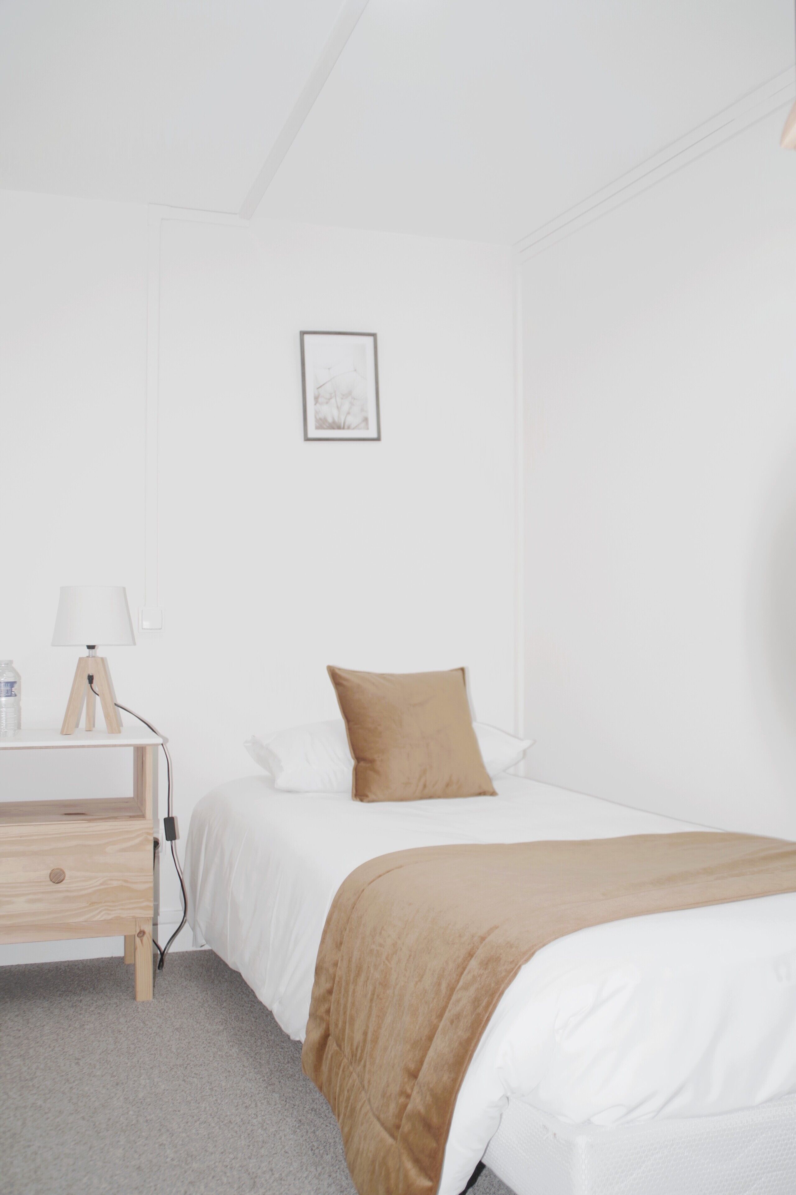 A minimalist hotel room with a single bed, a bedside table with a lamp, and a small bedside table with a water bottle.