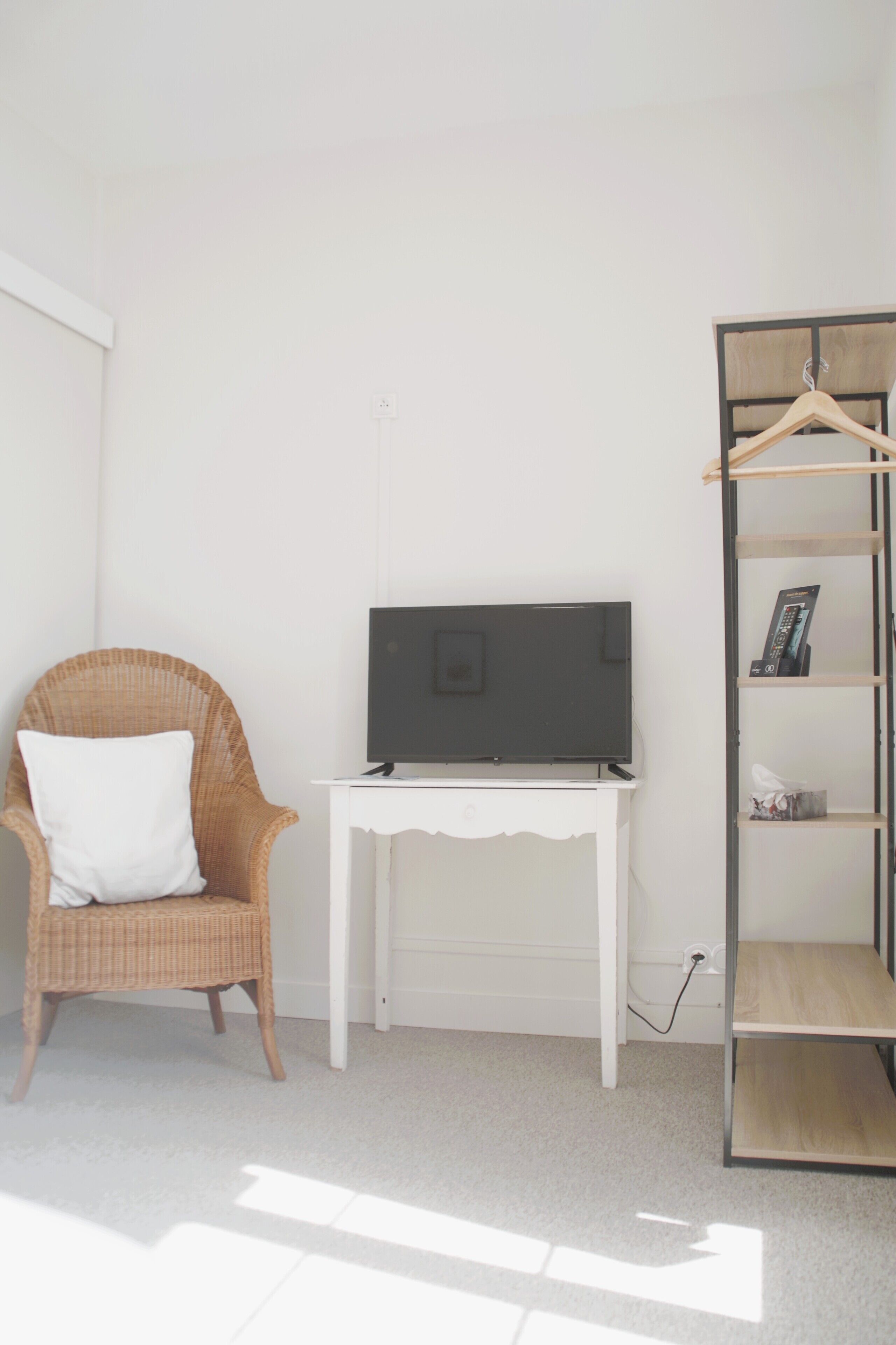 Een kamer met een rieten stoel, een witte tafel met een flatscreen televisie en een houten plankunit.