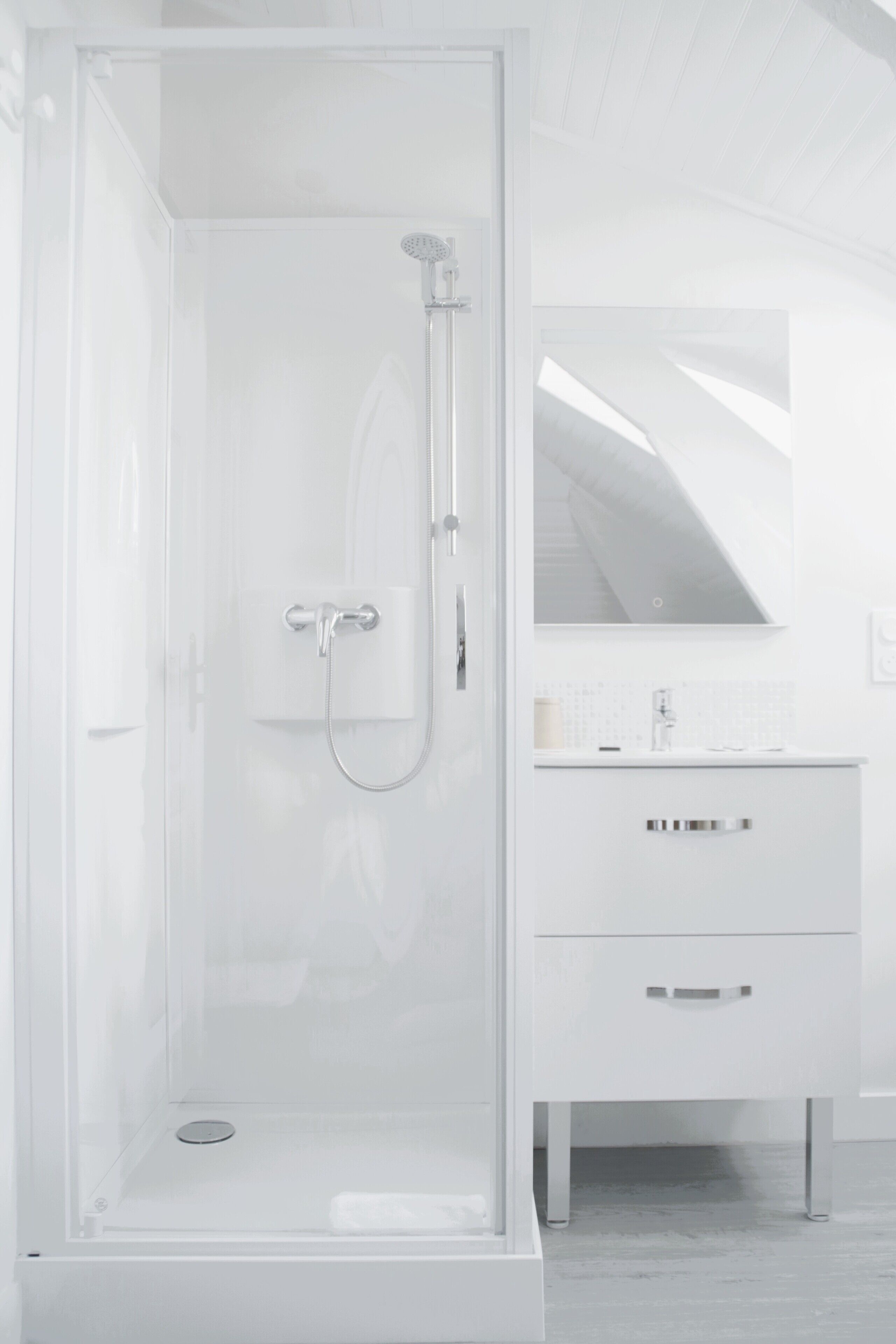 Une salle de bain moderne dotée d’une douche à parois de verre, d’un meuble-lavabo blanc avec un miroir et d’un design épuré et minimaliste.
