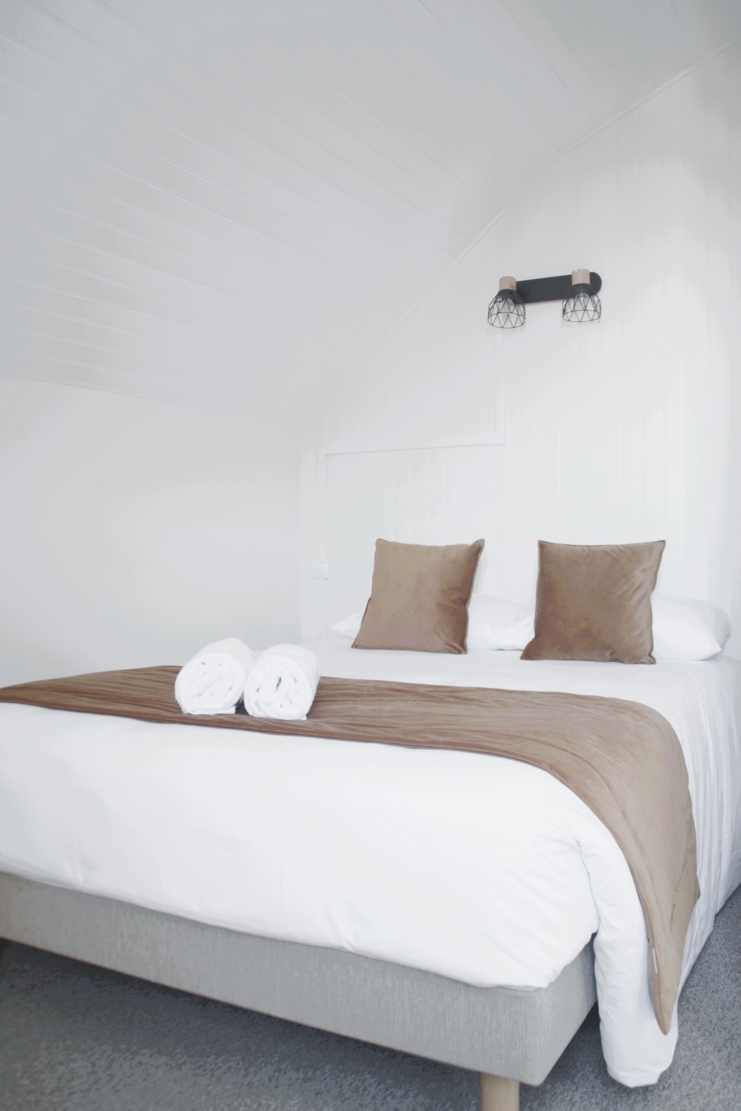 A modern hotel room with a neatly made bed, two pillows, and a wall-mounted light fixture.