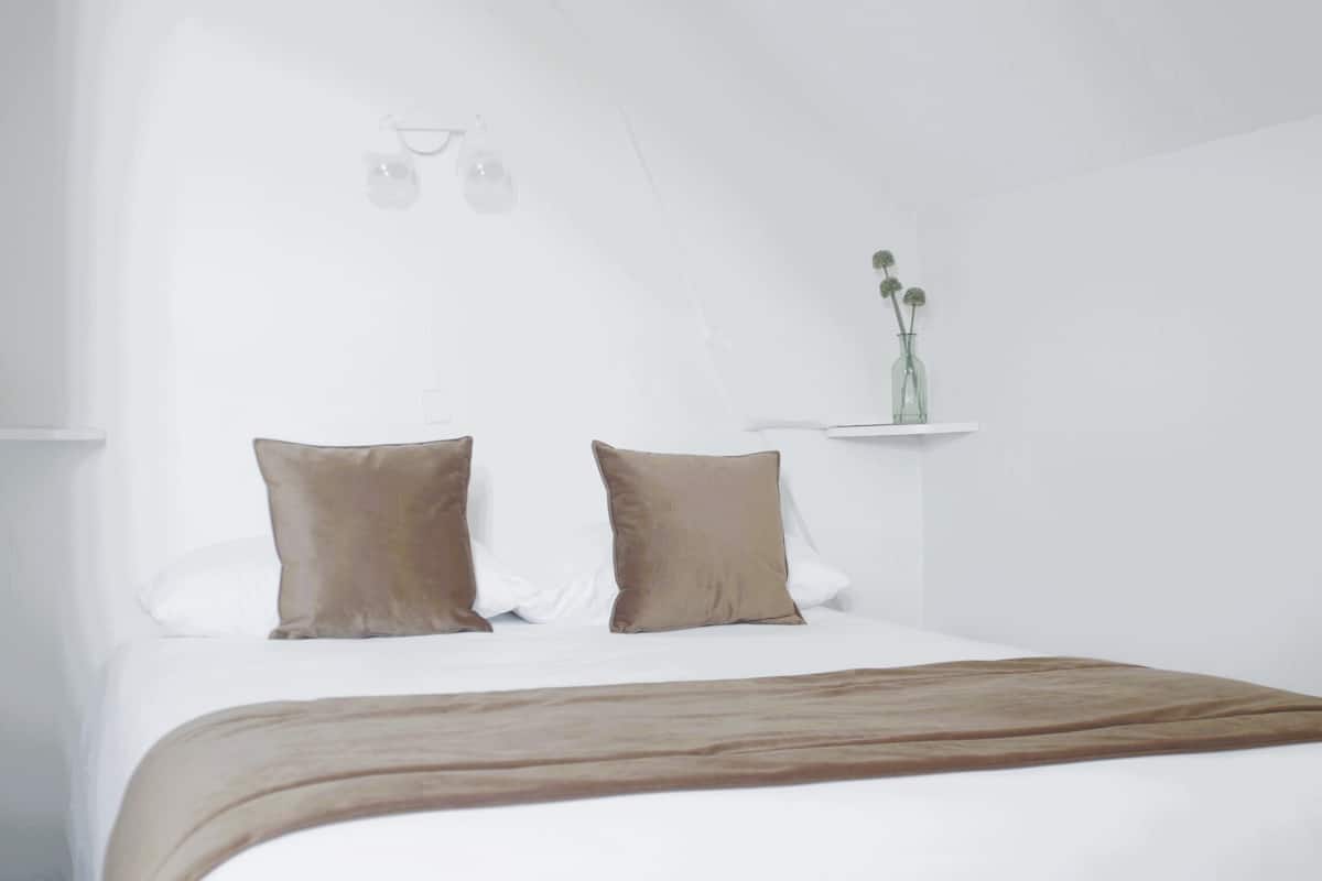 A bedroom with a bed, pillows, a bedside table, and a vase with flowers.