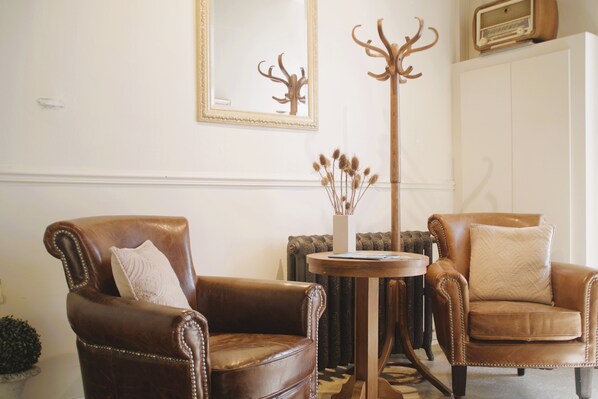 A room with two brown leather armchairs, a round wooden table, a tall floor lamp, and a mirror on the wall.