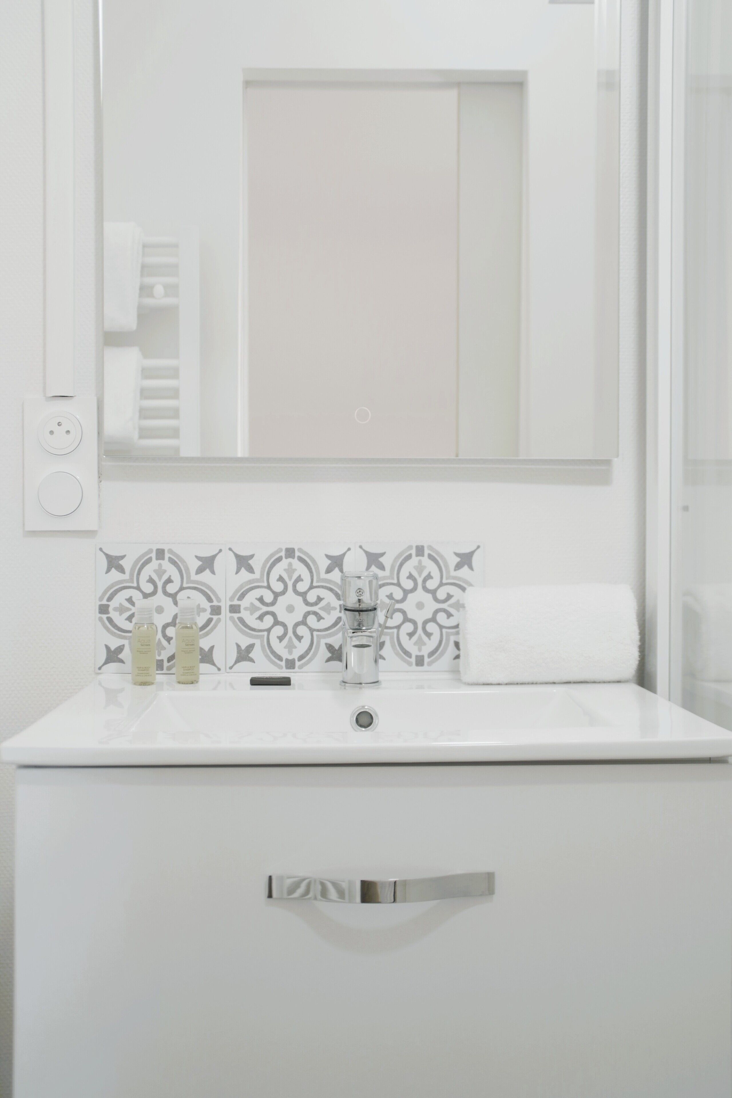 Une salle de bain avec un lavabo blanc, un miroir et un mur recouvert de carreaux décoratifs.