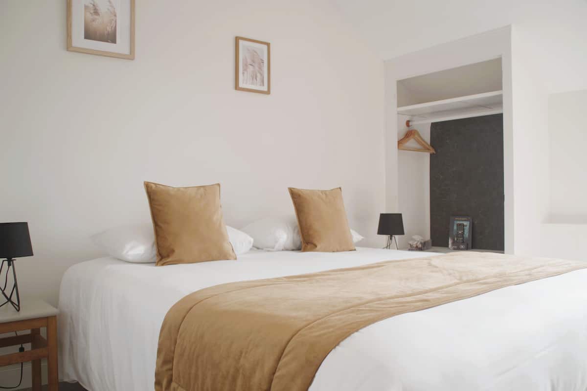 A neatly made bed with a beige blanket, two pillows, and a bedside table with a lamp.