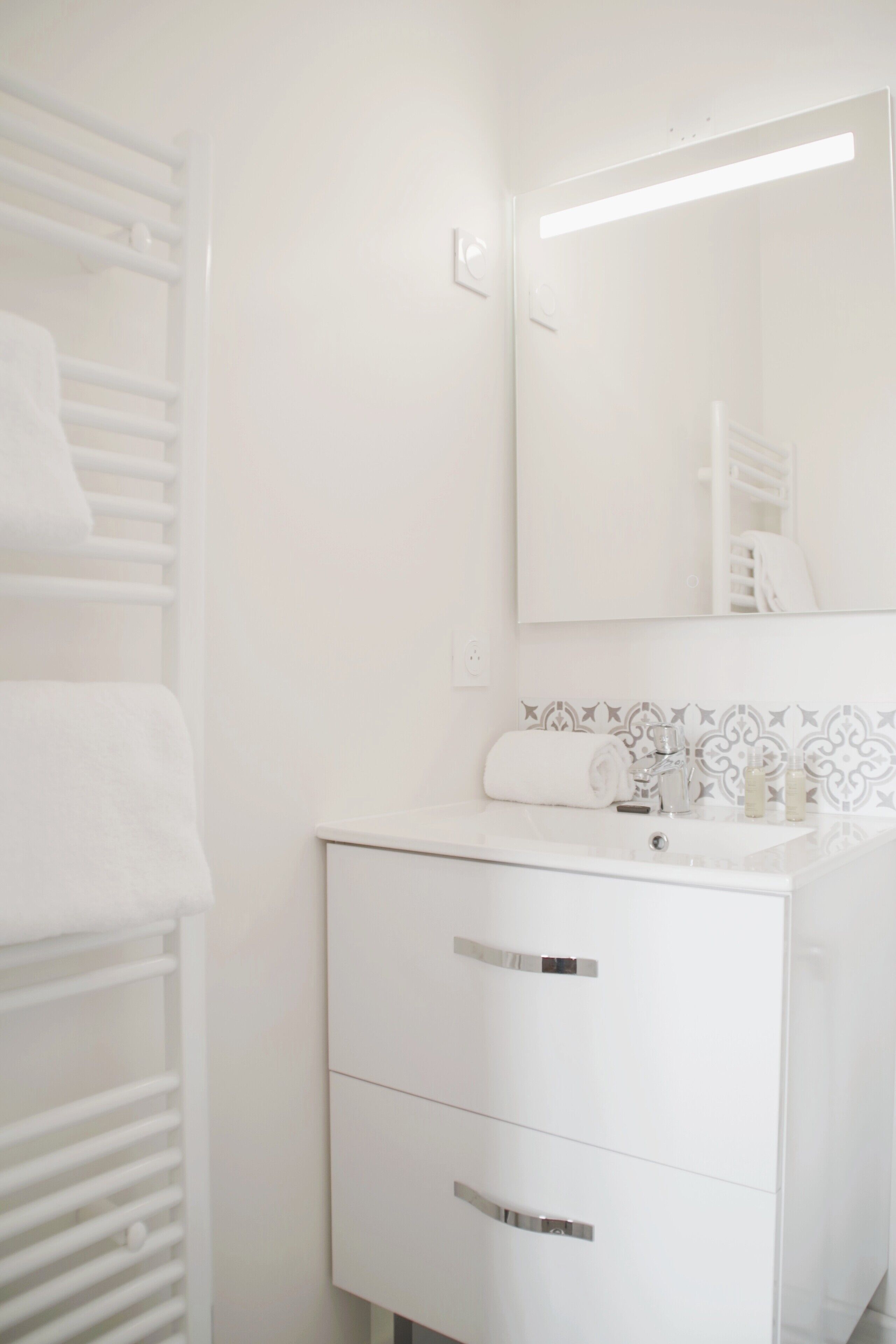 Een badkamer met een witte wastafel, twee lades, een spiegel en een handdoekhouder.