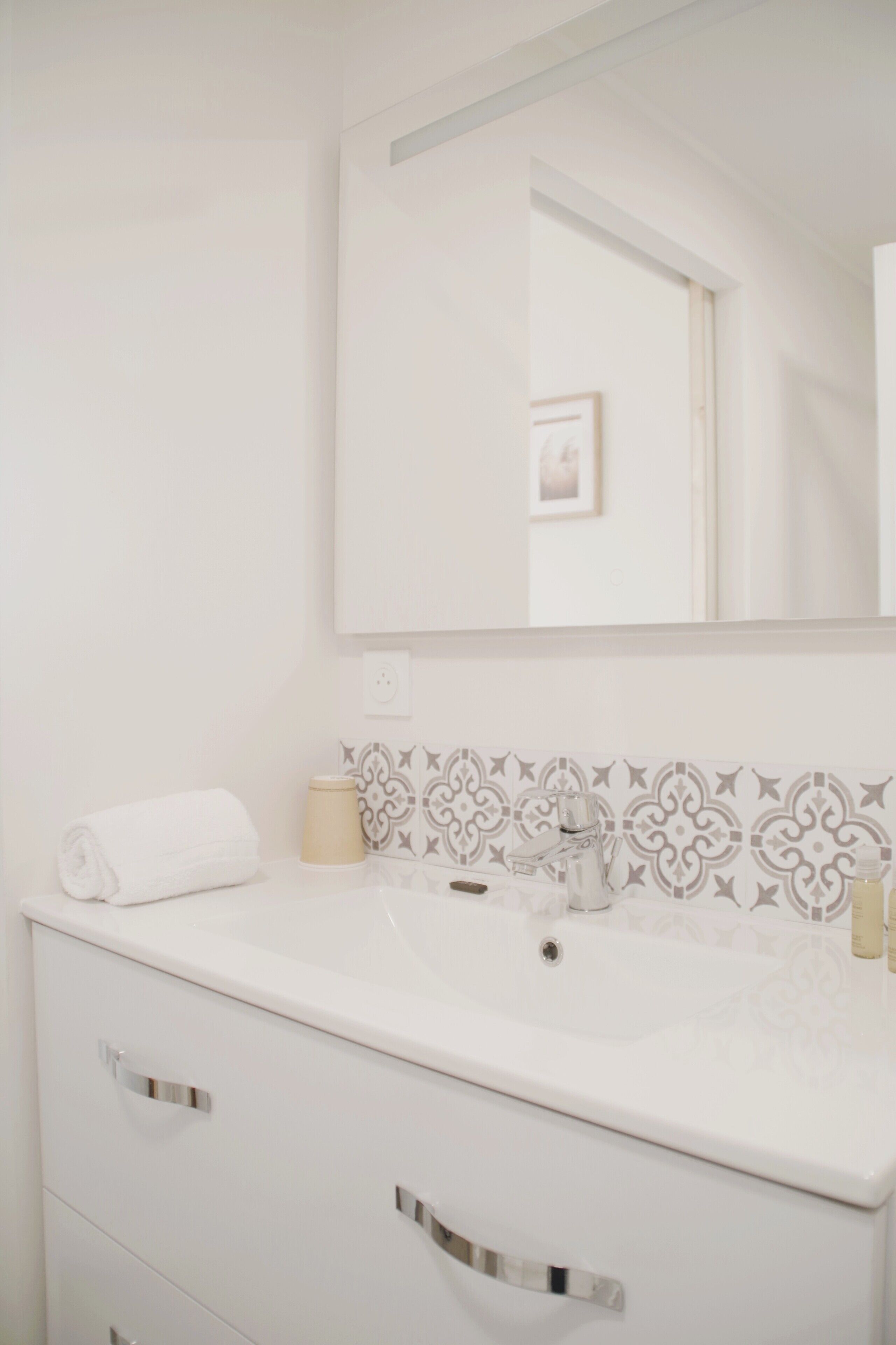 A bathroom with a white sink, a mirror, and patterned tiles on the wall.