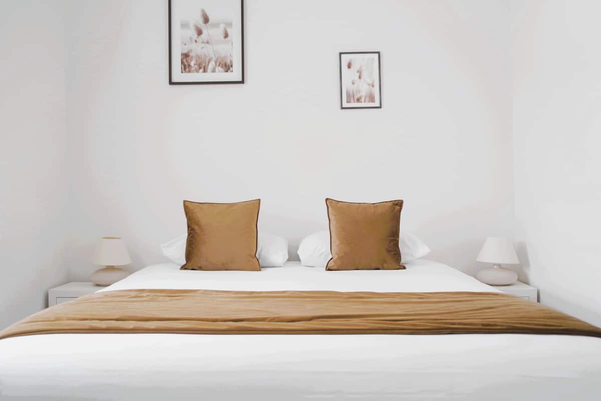 A neatly made bed with a brown blanket and two brown pillows, white bedding, and two bedside lamps on either side.