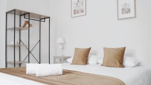 Una cama bien hecha con una colcha marrón y dos almohadas, un armario de madera, una mesita de noche con una lámpara y dos cuadros enmarcados en la pared.