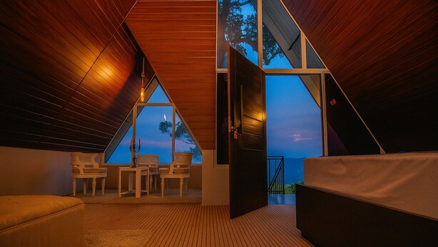 A modern bedroom with a sloped ceiling, large windows, and a view of the outdoors. - Hilltop Heaven Cabanas (CP)