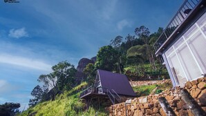 A stone house with a sloped roof, a metal staircase, and a view of a mountain. - Hilltop Heaven Cabanas (CP)