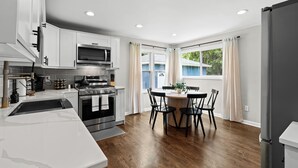 Een moderne keuken met witte kasten, roestvrijstalen apparatuur en een eethoek met een ronde tafel en stoelen.