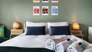 A neatly made bed with white and navy blue pillows, a dark green blanket, and rolled white towels on a wooden nightstand. - City Centre | Top Floor w/ Balcony & Sunset Views | Pass the Keys (Belfast)