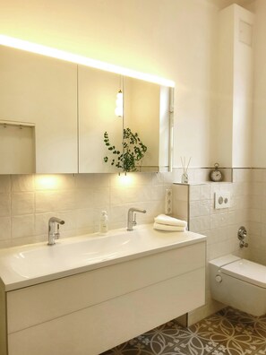 Ein modernes Badezimmer mit einem Doppelwaschbecken, einem Spiegel, einer Uhr und einer Toilette.