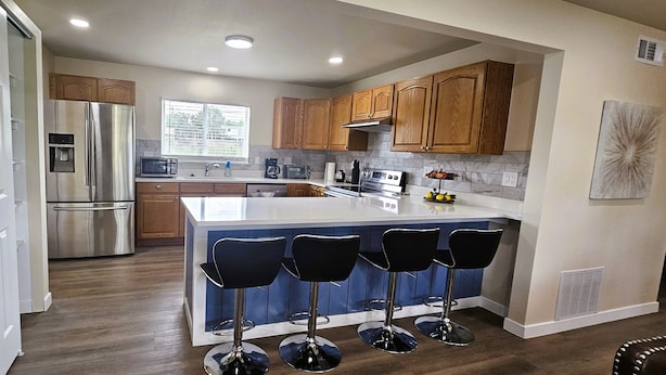 Una cocina moderna con armarios de madera, electrodomésticos de acero inoxidable, una isla central con taburetes y una ventana que proporciona luz natural.