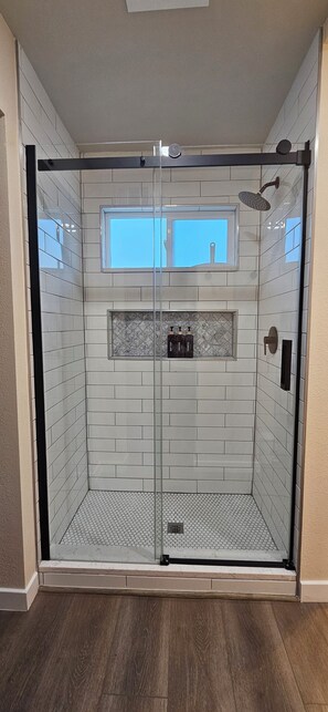 A walk-in shower with a glass door, a small window, and a tiled floor.
