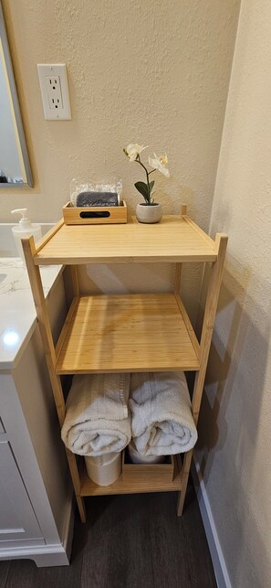 A wooden shelf unit with a towel, a potted plant, and a glass container in a bathroom.