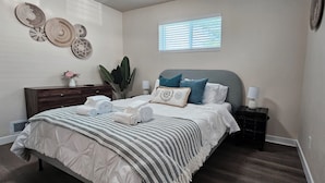 Un dormitorio con cama, mesitas de noche, cómoda, ventana y decoración en la pared.