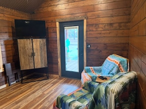 A wooden cabin interior with a sofa, a cabinet, and a door leading outside. - Blackberry Bungalow,,Cozy cabin in charming Longview with WiFi, AC , a (Longview)