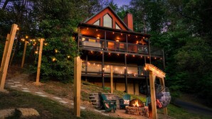 A two-story cabin with a balcony, outdoor seating, and a fire pit.