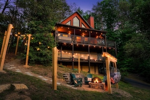 A two-story cabin with a balcony, outdoor seating, and a fire pit.