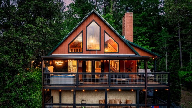 A two-story cabin with a balcony, large windows, and a chimney.