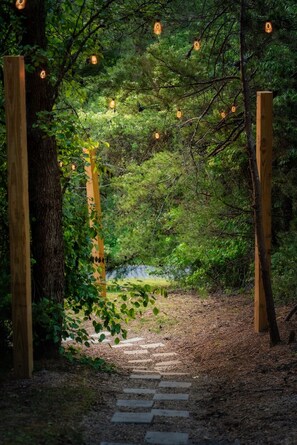 A wooden pathway leading through a forested area with a wooden archway and string lights.