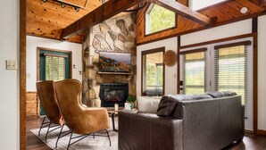 A cozy living room with a stone fireplace, leather furniture, and large windows.