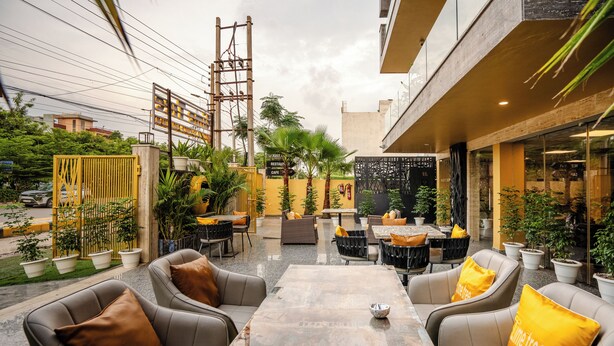An outdoor seating area with tables and chairs, surrounded by potted plants and a yellow fence. - Lime Tree Hotel Medanta (Gurugram)