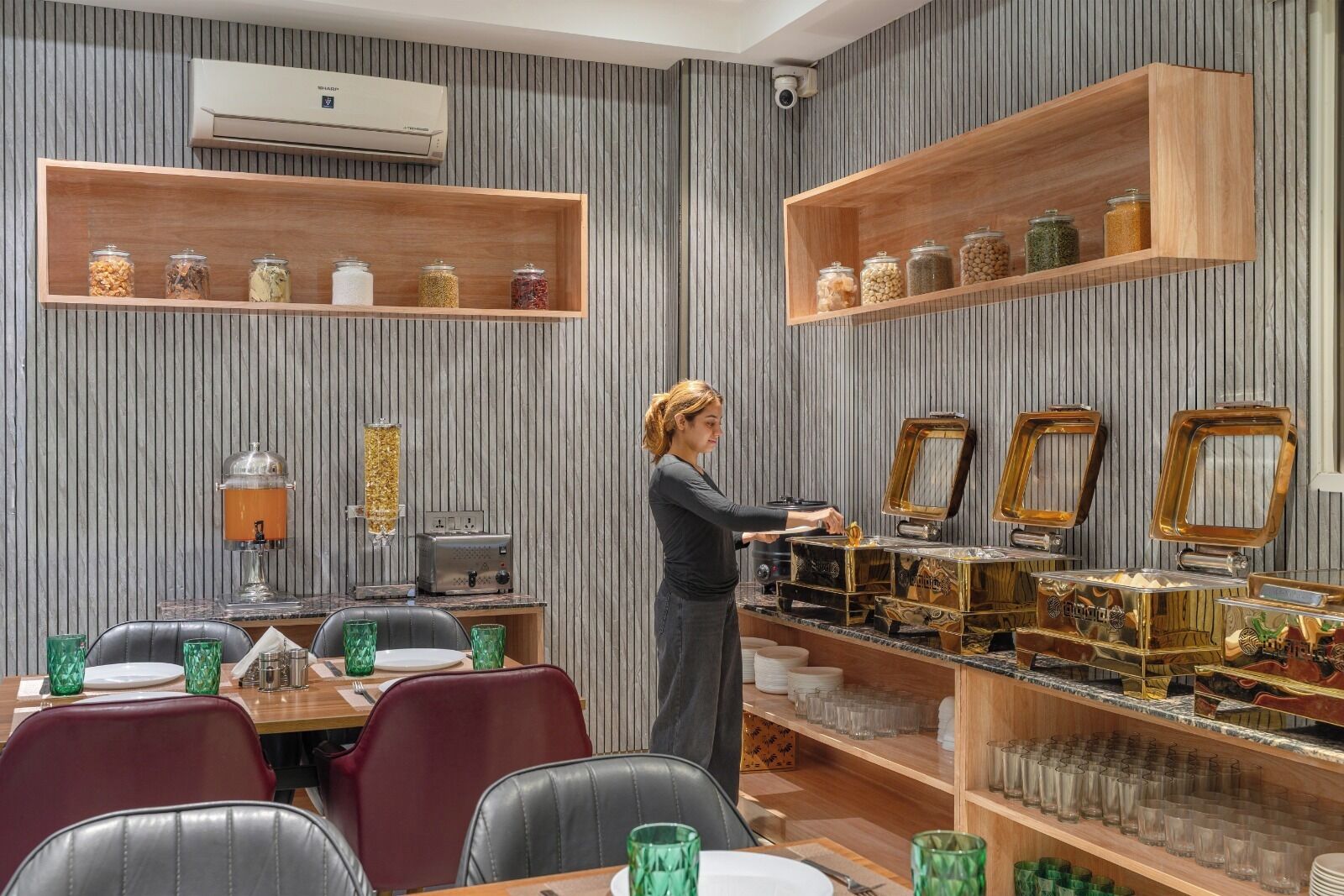 A restaurant with striped wallpaper, wooden shelves with jars, a coffee machine, and a person serving.