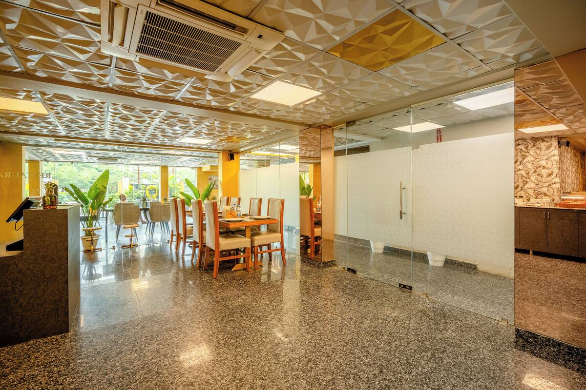 A modern interior with a geometric ceiling design, a central dining area with chairs and a table, and a view through large windows.