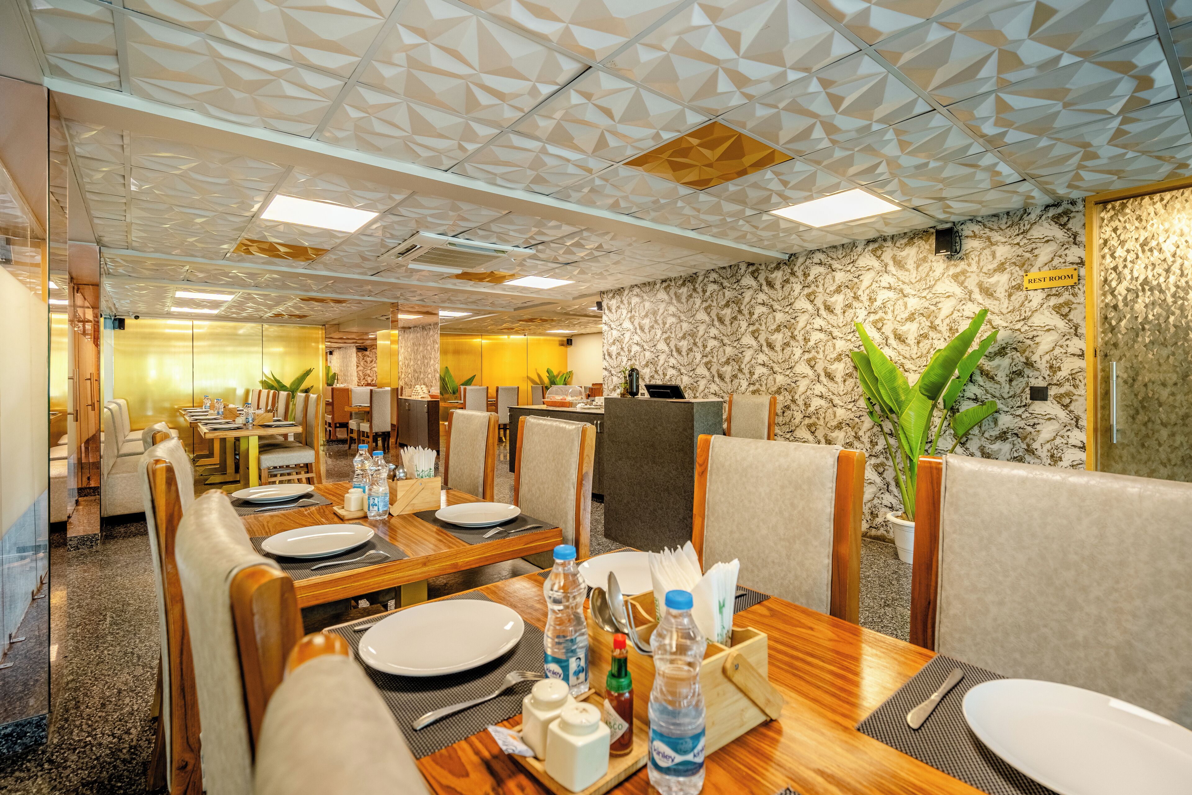A dining area with tables set for four, equipped with plates, cutlery, and bottled water.