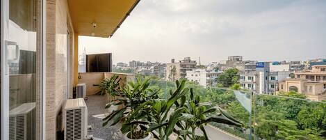 Un balcón con plantas en macetas, unidades de aire acondicionado y vistas a un paisaje urbano.