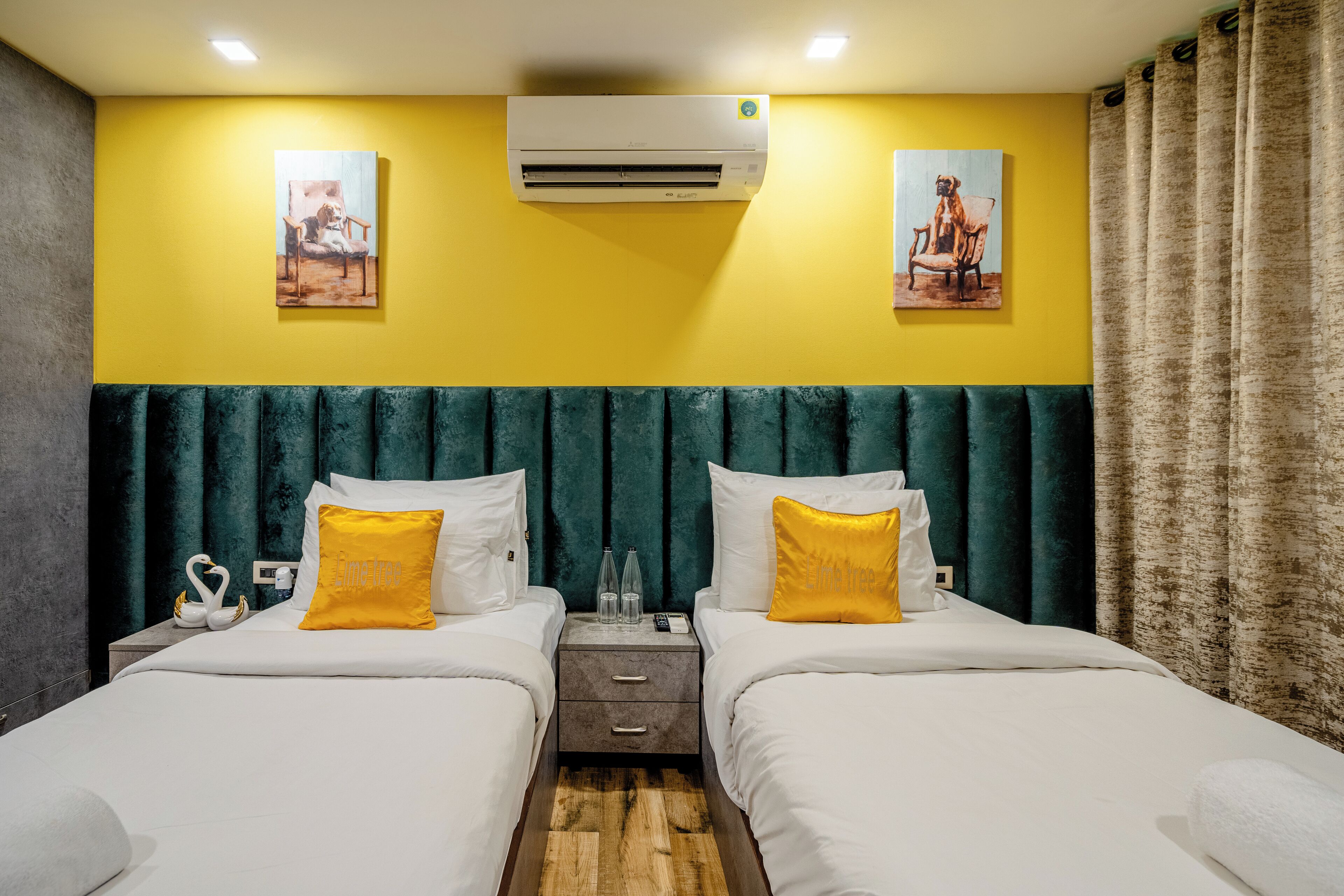 A hotel room with two beds, a green headboard, yellow walls, and artwork above the beds.
