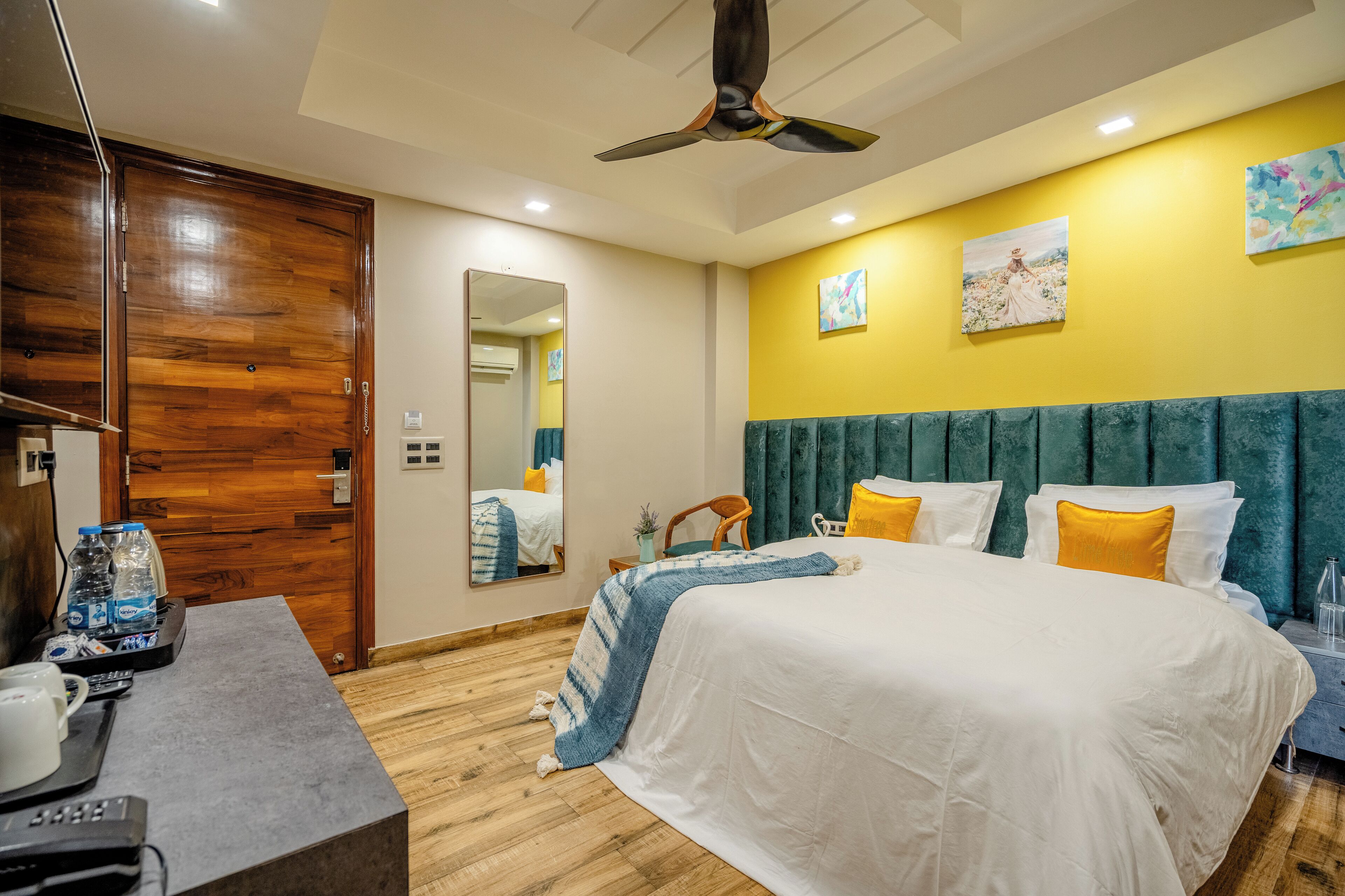 A hotel room with a bed, a desk with a telephone and water bottles, a ceiling fan, and artwork on the wall.